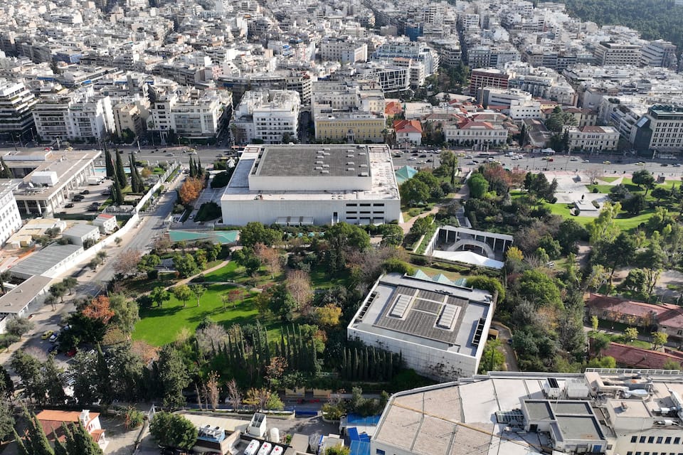 An aerial view of a cityscape with dense urban buildings, a large open park, and a prominent white building with a green roof.