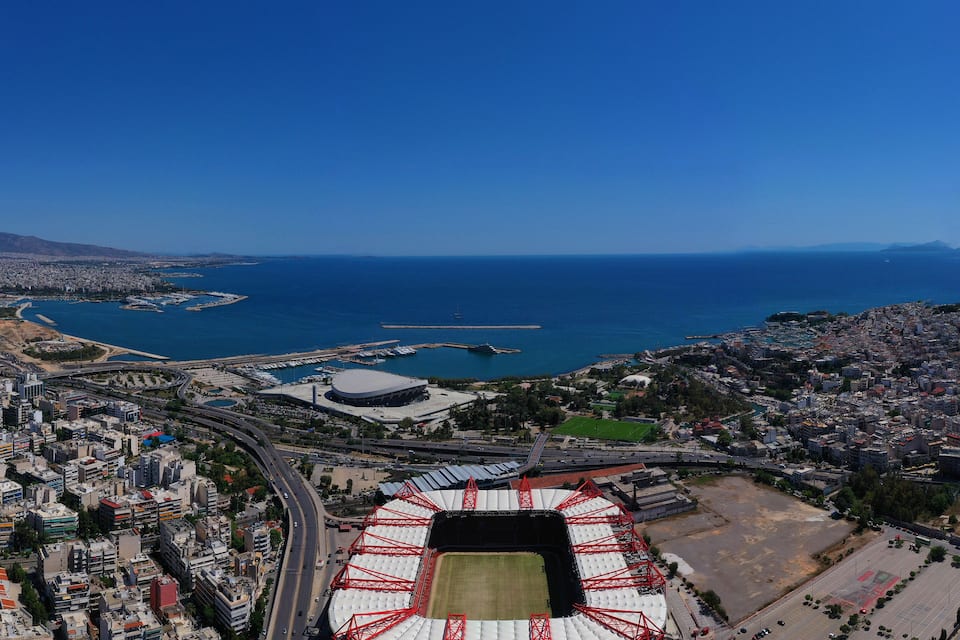 Luchtbeeld van een kuststad met een groot stadion, een jachthaven en een dichtbevolkt stedelijk gebied.
