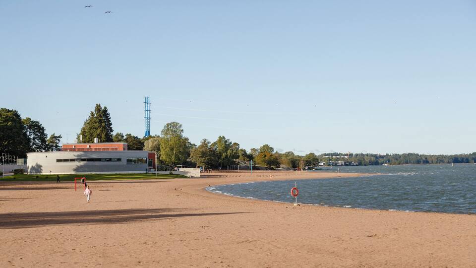 A sandy beach with a lifebuoy, a clear sky, and a building in the background.
