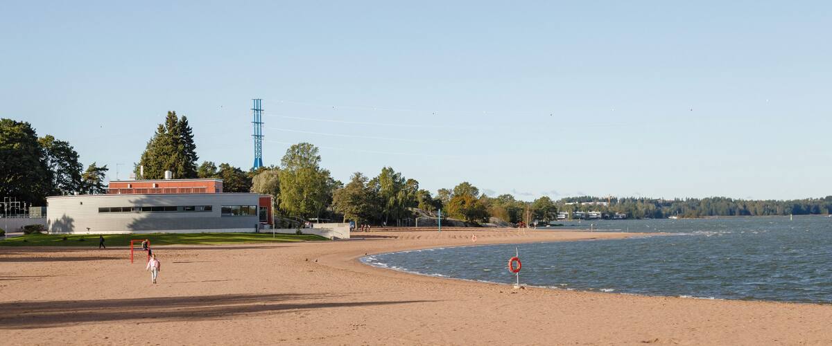 A sandy beach with a lifebuoy, a clear sky, and a building in the background.