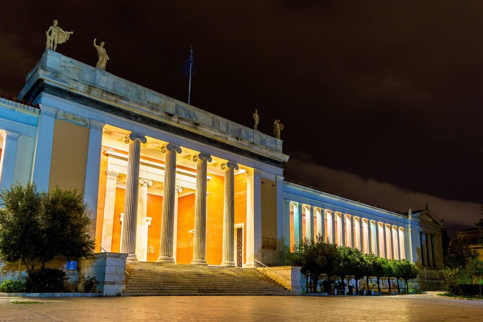 A classical building with columns and statues, illuminated at night.