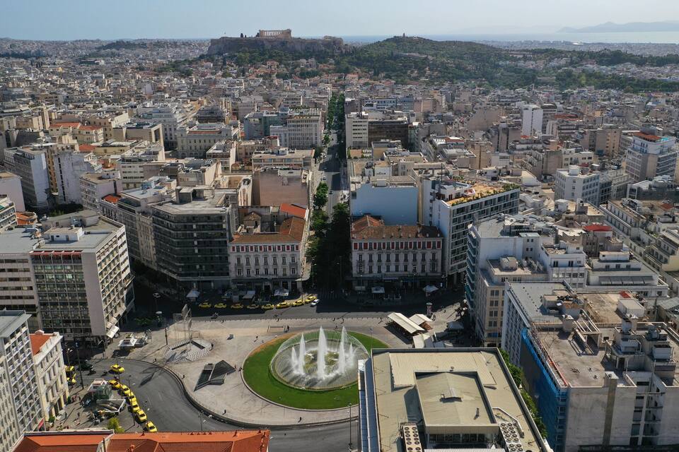 A cityscape with a prominent roundabout, historic buildings, and a distant view of a hill with ruins.