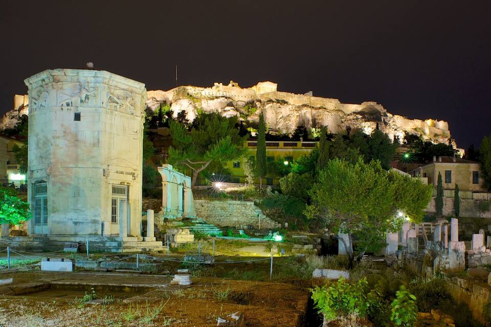 Une ruine antique, avec une grande colonne et un escalier en pierre, entourée d’arbres et d’un petit étang.