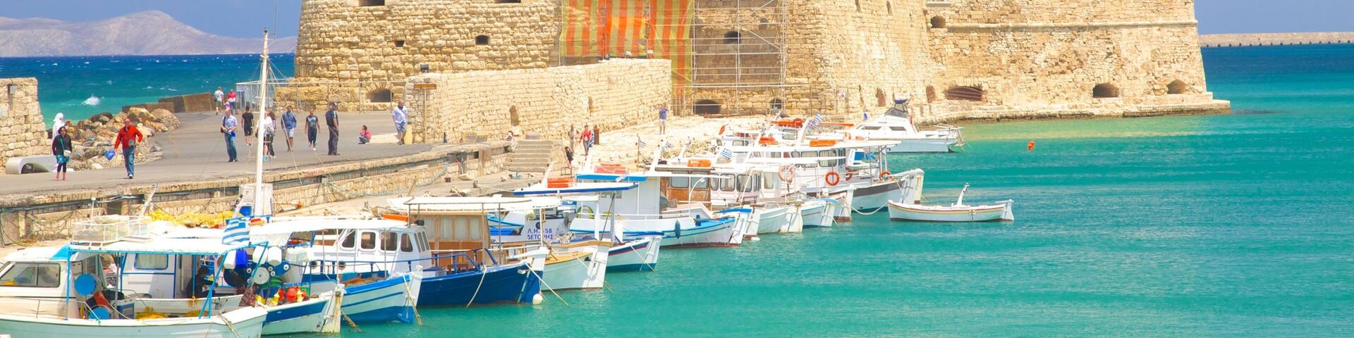 A historic stone fortress by the sea with boats docked in front.