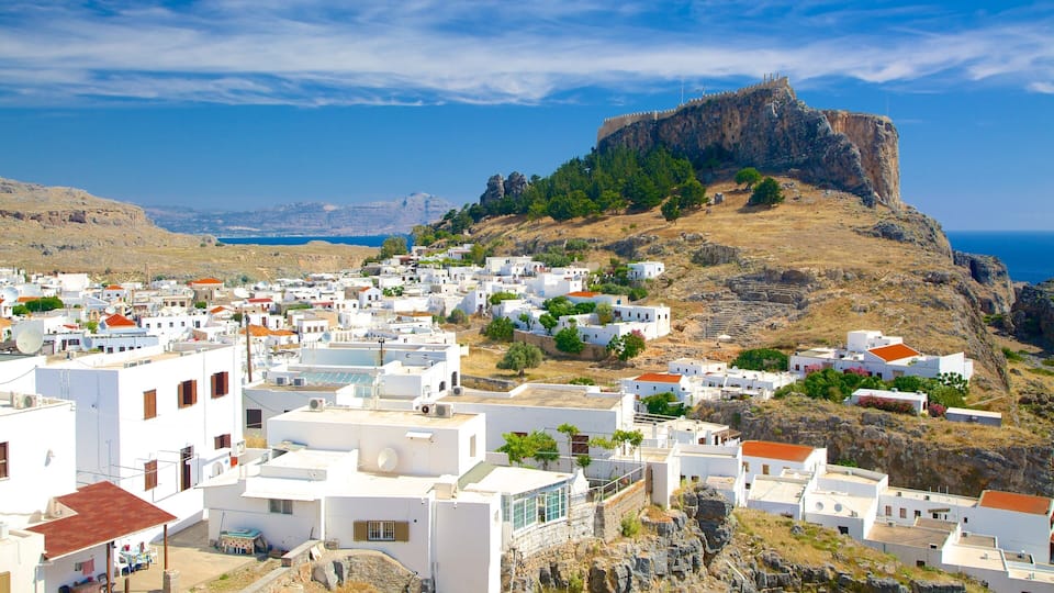 A coastal town with white buildings, a rocky hill with a fort, and the sea in the background.