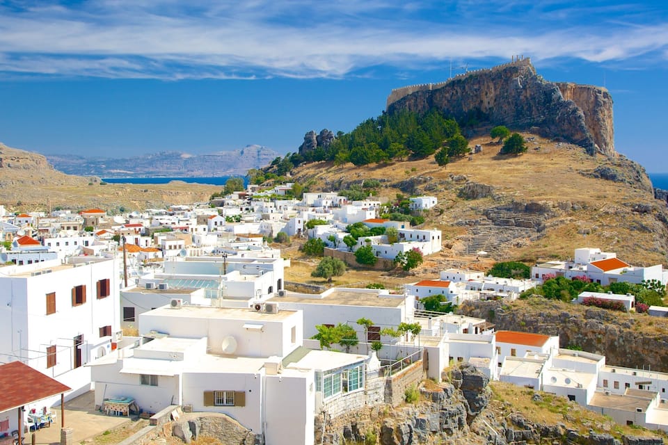 A coastal town with white buildings, a rocky hill with a fort, and the sea in the background.