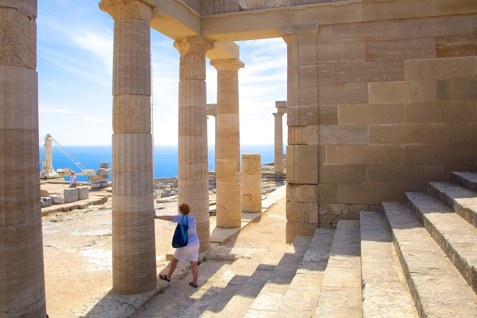 Ancient stone columns and steps at a historical site with a view of the sea in the background.