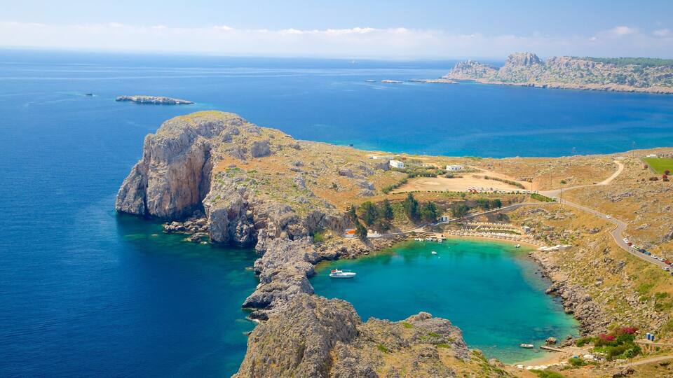 A coastal landscape with rocky cliffs, clear blue waters, and a small settlement with buildings and a road.