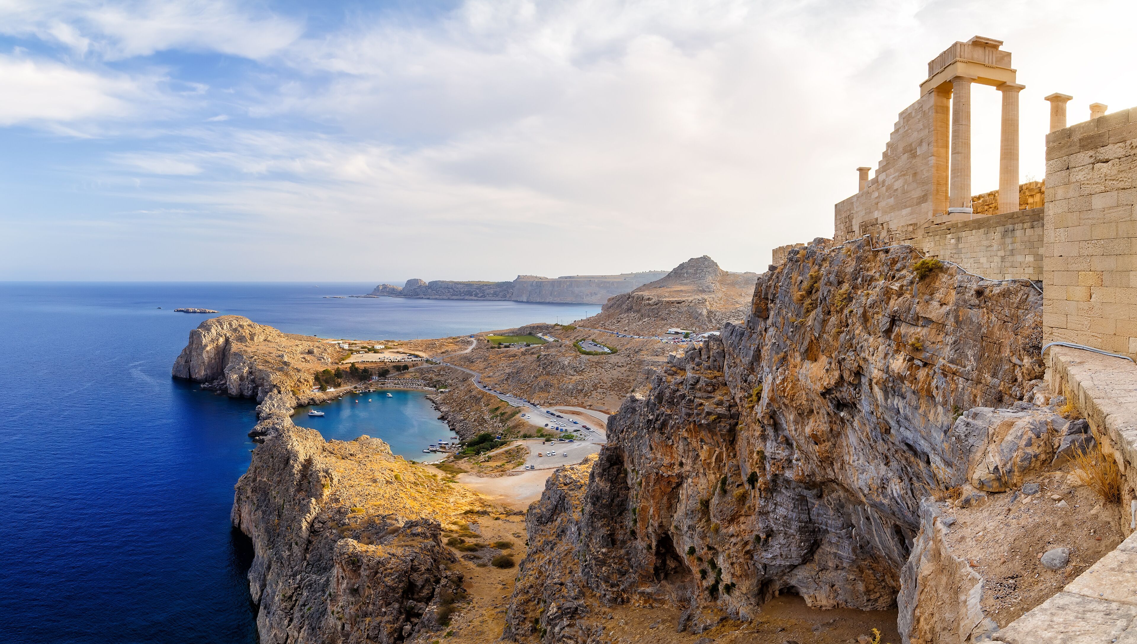 A coastal cliff with a historic stone structure, a rocky bay, and a clear view of the sea.