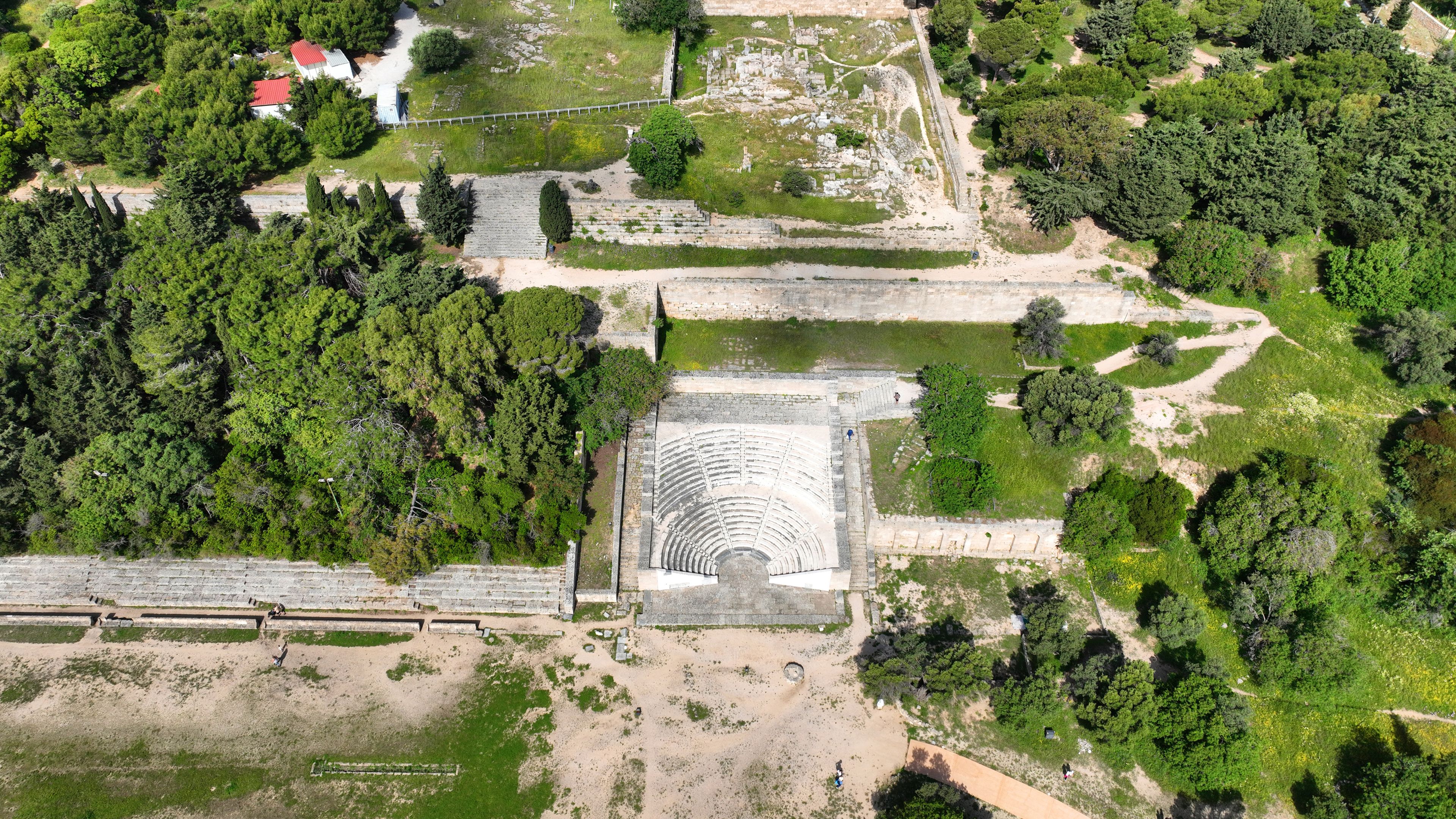 An ancient amphitheater surrounded by dense forest and ruins.