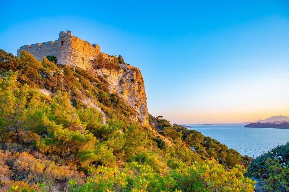 A historic stone castle on a hill overlooking a calm sea.