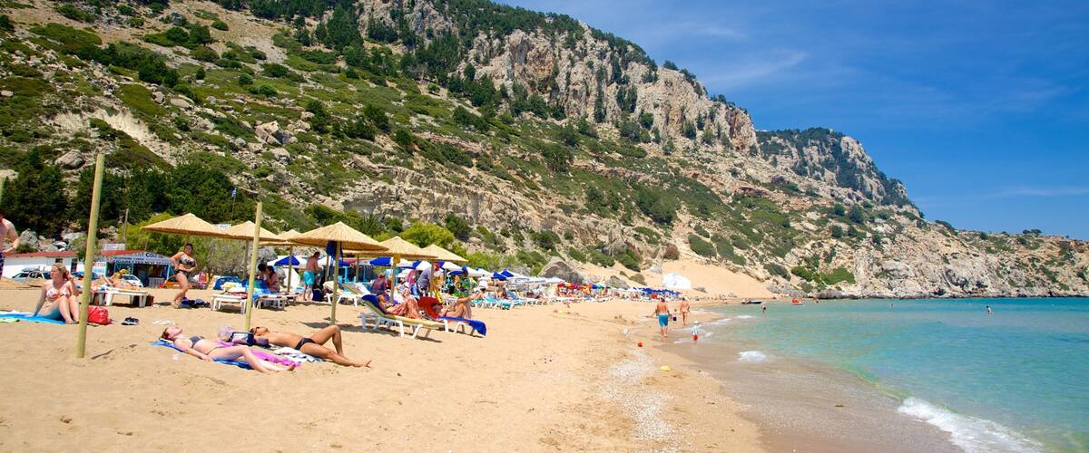 A beach with people sunbathing, umbrellas, and a rocky mountain in the background.
