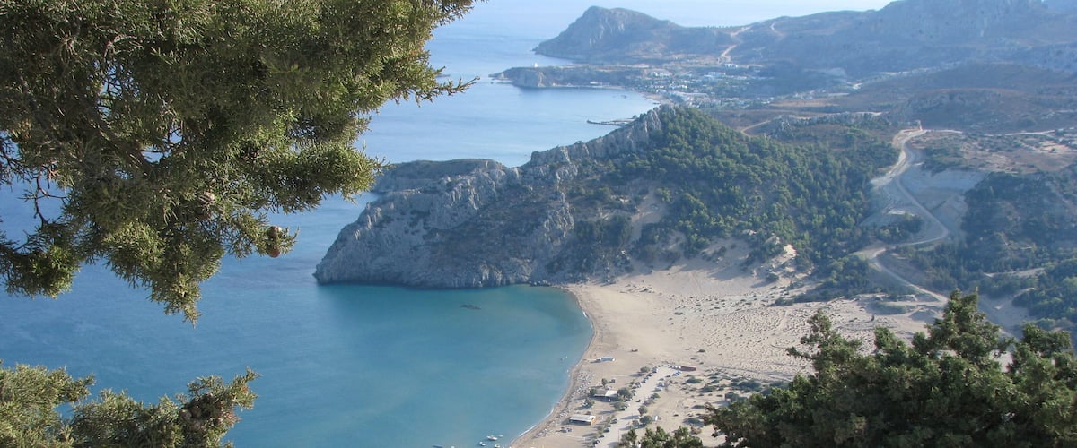 A coastal landscape with a beach, rocky cliffs, and a clear blue sea.