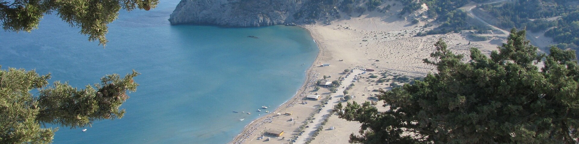 A coastal landscape with a beach, rocky cliffs, and a clear blue sea.