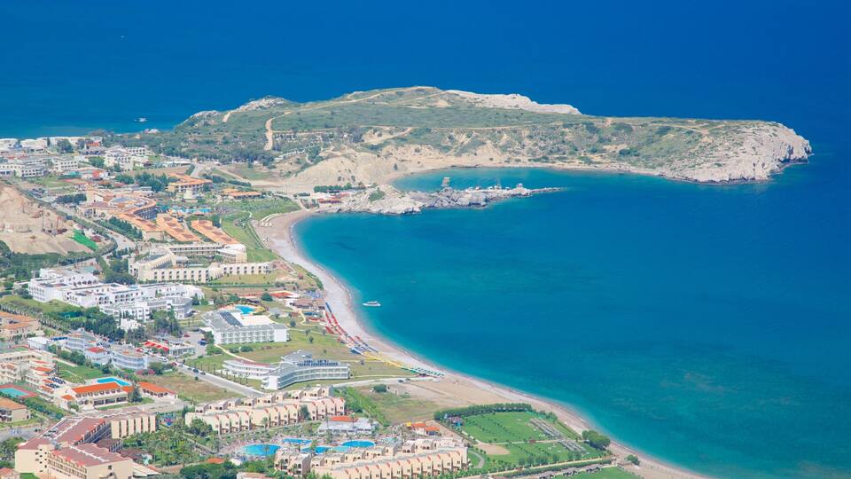 An aerial view of a coastal town with a beach, buildings, and a rocky hill.