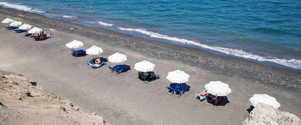 A beach with rows of blue chairs and white umbrellas, and people swimming in the ocean.