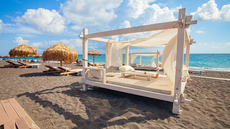 A beach with a wooden bed structure, lounge chairs, and thatched umbrellas.
