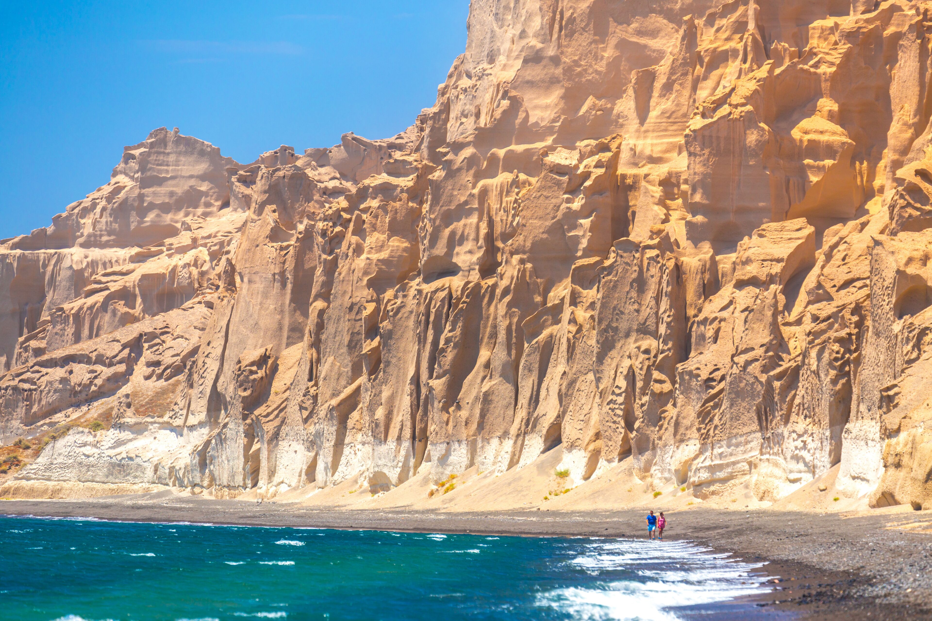 A rocky coastline with clear blue waters and a person walking on the beach.