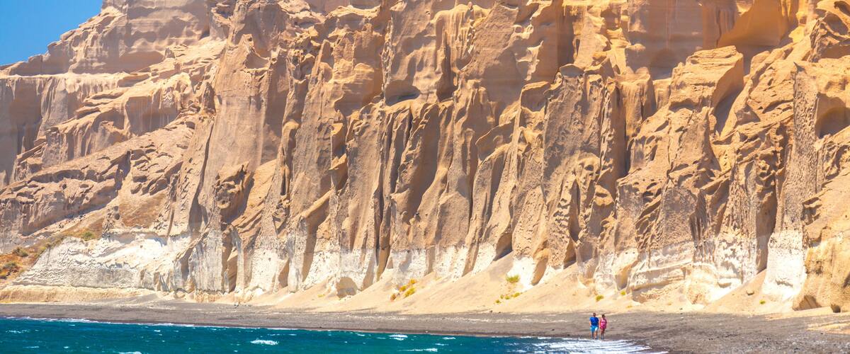 A rocky coastline with clear blue waters and a person walking on the beach.