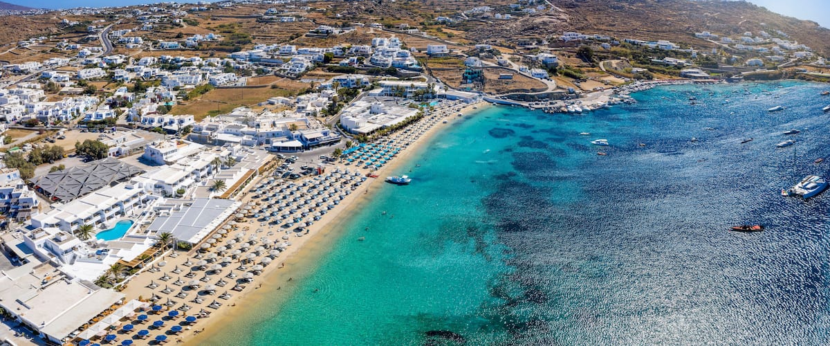 Panoramic aerial view to the popular beach of Ornos, Mykonos island, Greece, with turquoise sea and sun umbrellas lined up on the fine sand