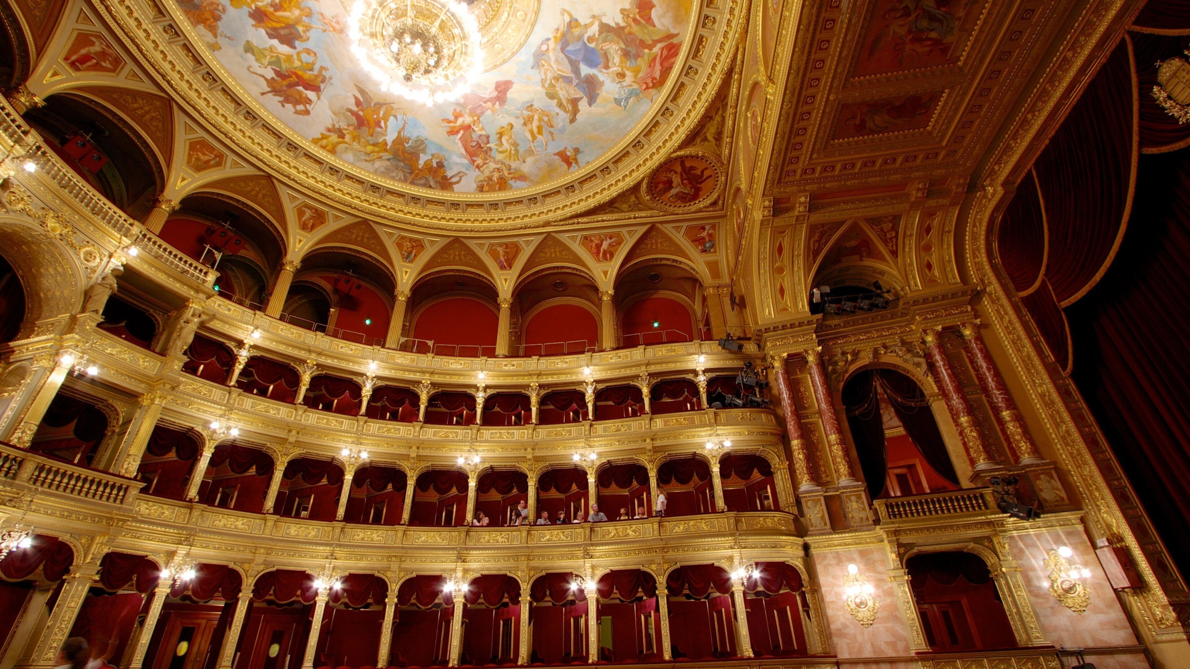 A grand theater with ornate golden decorations, multiple balconies, and a detailed ceiling fresco.