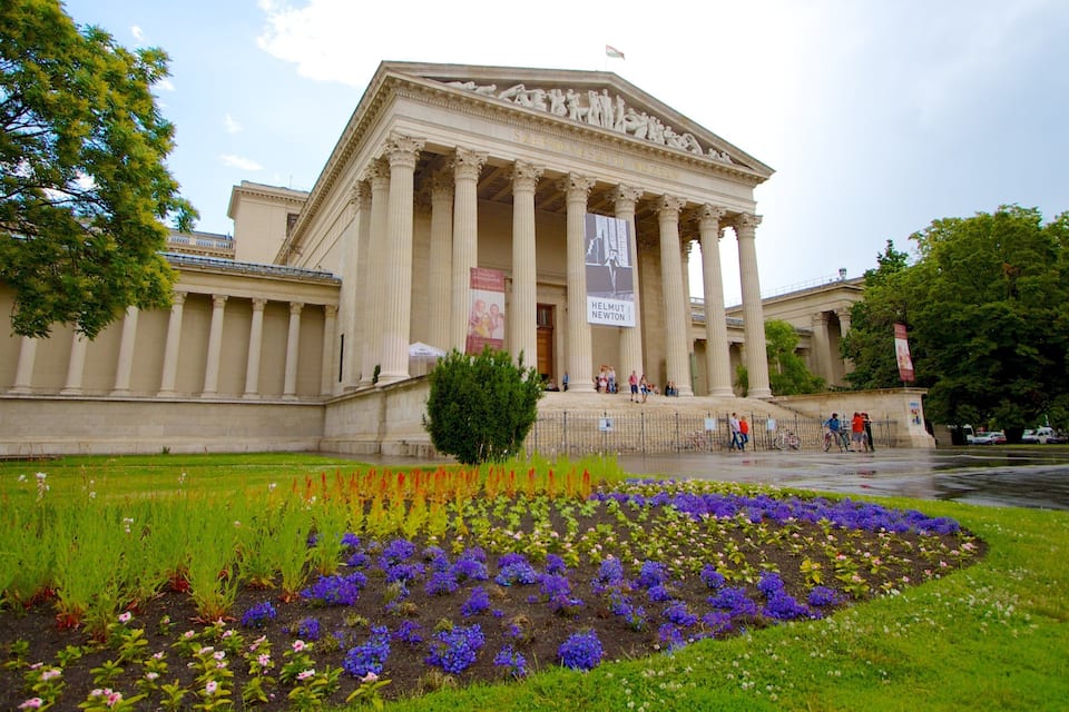 Un edificio neoclassico con colonne, circondato da un giardino fiorito di fiori viola.