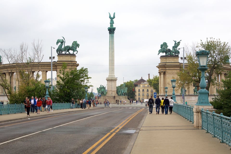 A large monument with statues of horses and an angel on top, surrounded by a bridge and a crowd of people.