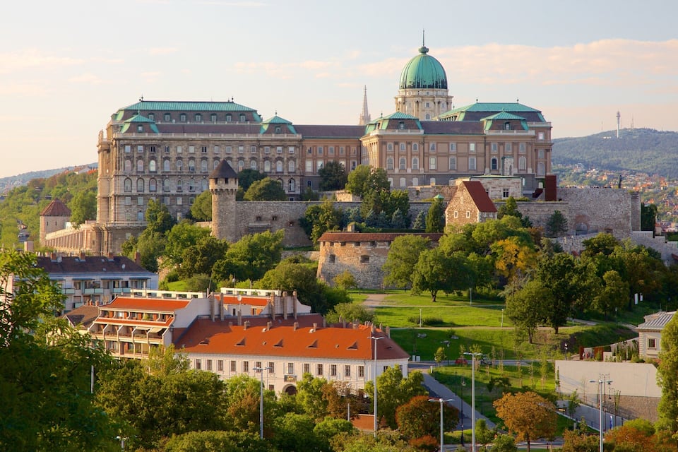 A historic castle with a green dome and red-roofed buildings in a lush, green valley.