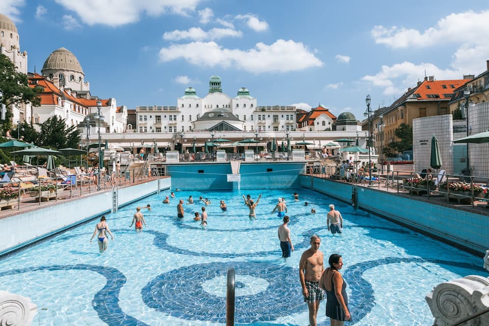 Ein Schwimmbecken mit Personen, umgeben von Gebäuden und einer großen Kuppelkonstruktion.