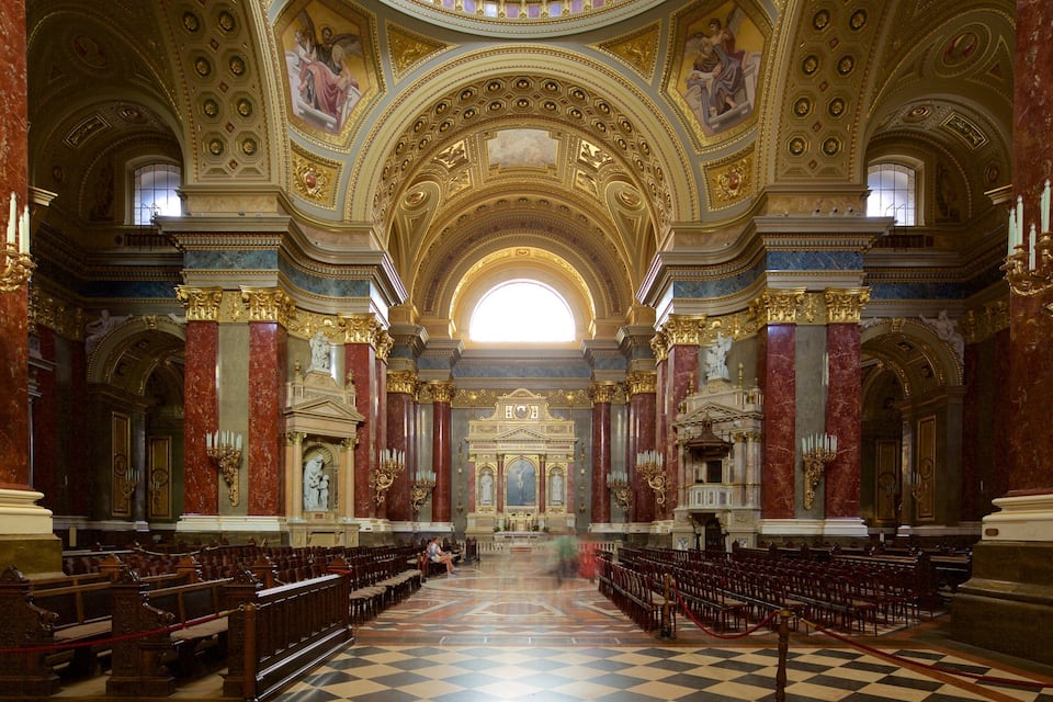 An ornate church interior with high ceilings, gold accents, and a checkered floor.