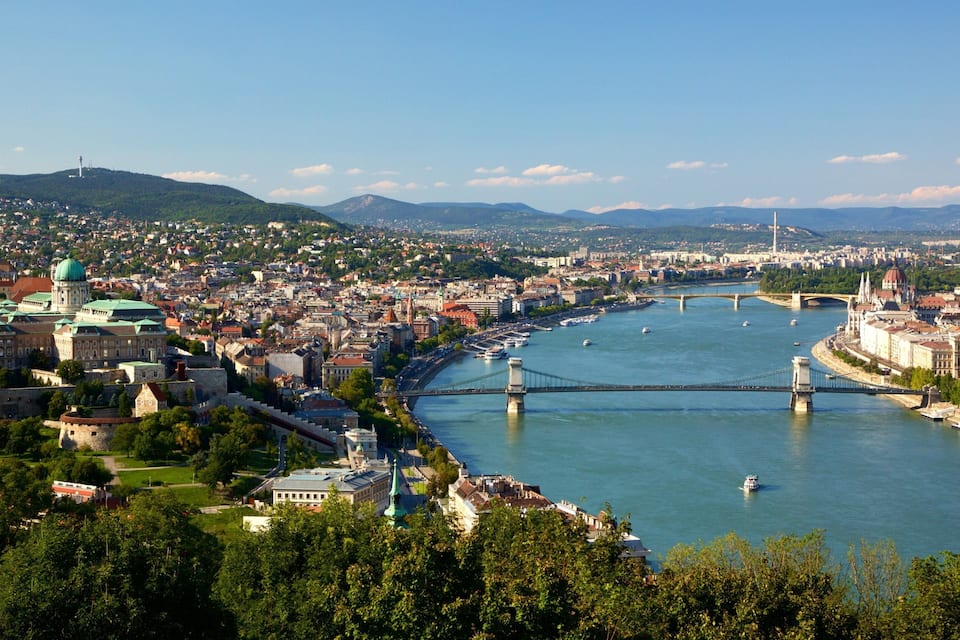 Ein Fluss mit Brücken, eine Stadtansicht und ein markantes Gebäude mit grüner Dachbegrünung.