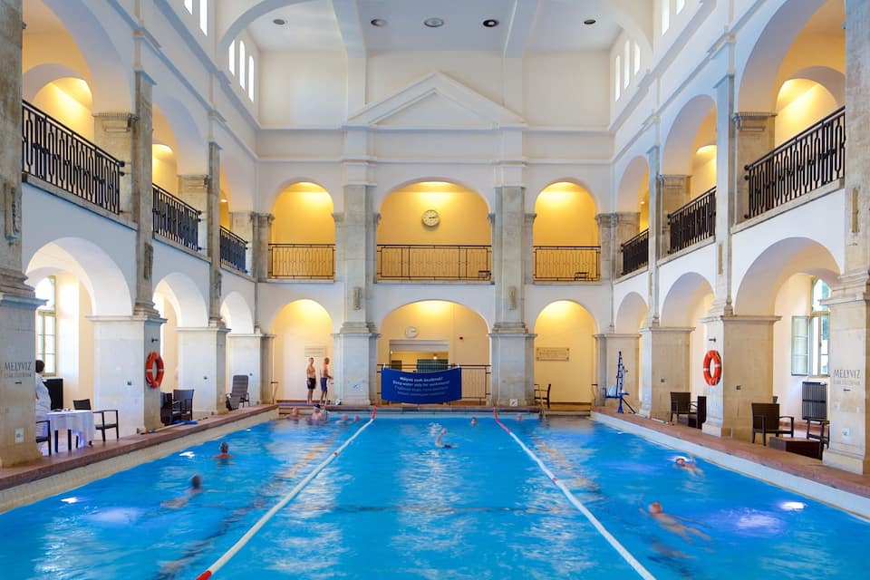 Ein hallenbad mit mehreren Bahnen, umgeben von klassischer Architektur mit Bögen und Säulen.