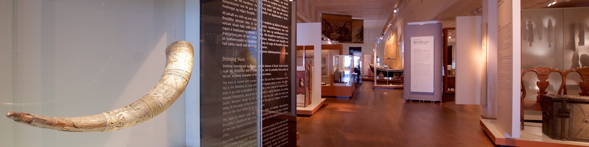 Exposição de museu com um chifre de beber grande e ricamente esculpido, além de painéis informativos.