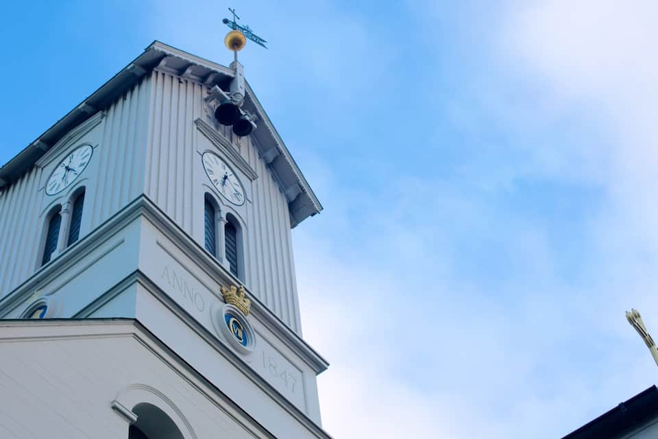 A church tower with a clock, a weather vane, and a crown symbol.