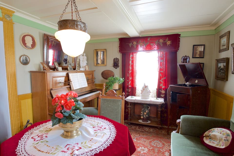 Une pièce avec un piano, une table ornée d’un vase de fleurs et un fauteuil vert.