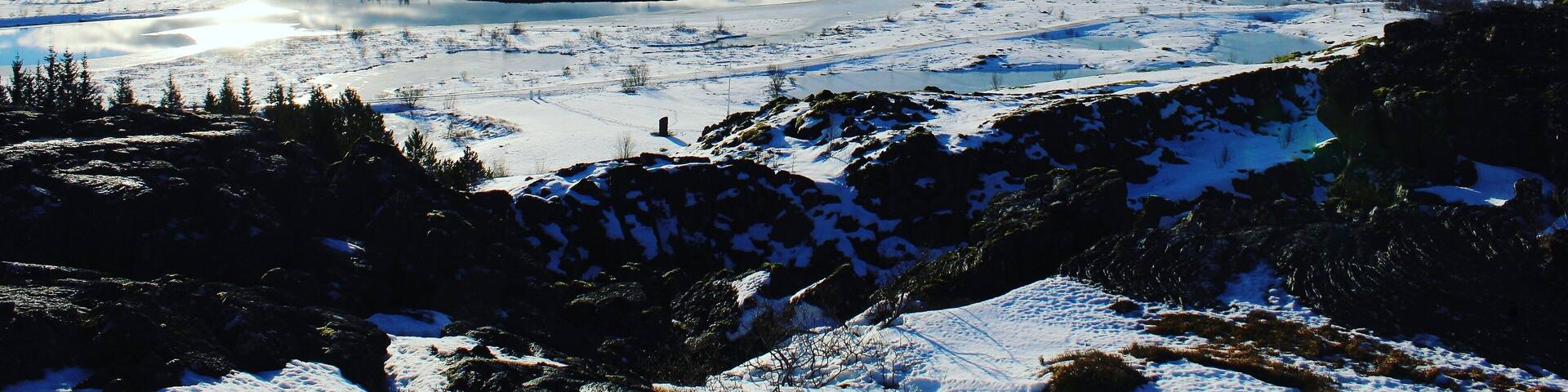A snowy landscape with a lake, mountains, and a partly cloudy sky.
