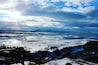 Un paisaje nevado con un lago, montañas y un cielo parcialmente nublado.