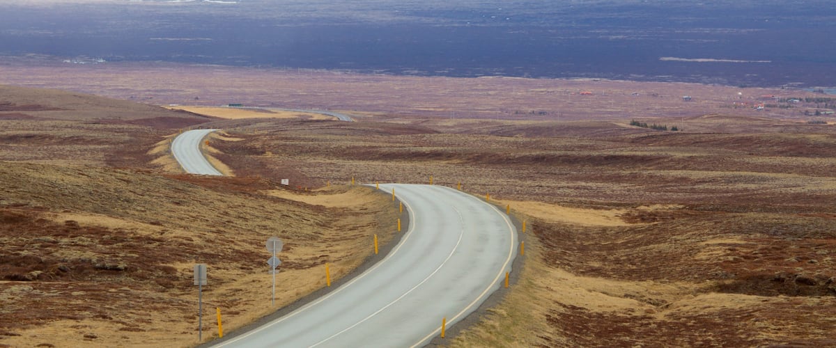 A winding road through a barren landscape with distant snow-capped mountains.