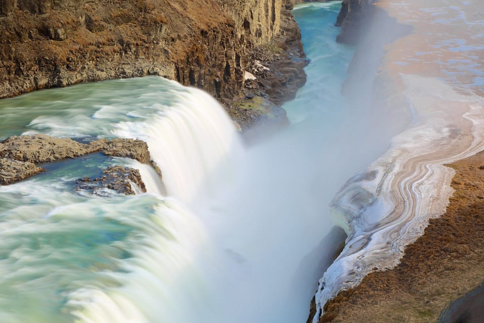 A waterfall cascading down a rocky cliff into a river, surrounded by a sandy beach with tide pools.