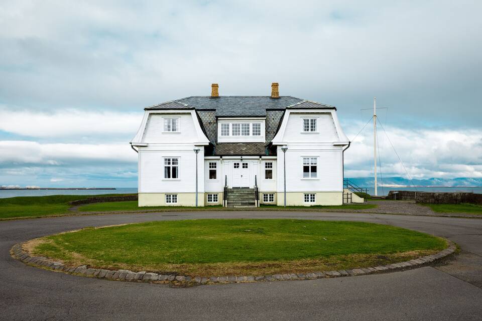 Een wit huis met een stenen dak, een vlaggenmast en een gazon.