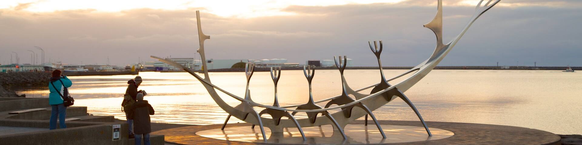 A sculpture of intertwined forks by the water at sunset.