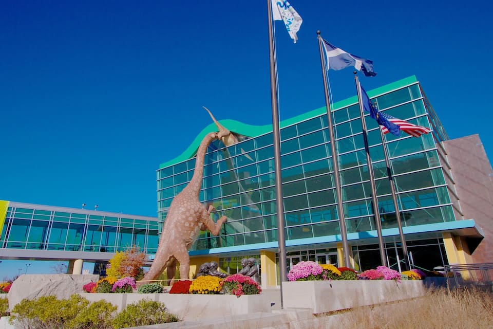 A modern building with a giraffe statue, multiple flags, and colorful flower beds.