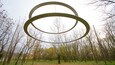 Eine runde Metallskulptur in einem Park mit kahl stehenden Bäumen und einer Rasenfläche.