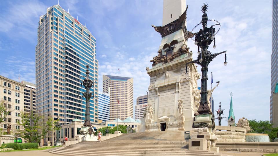 Uma praça urbana com um monumento imponente, arranha-céus modernos e uma estátua de um homem a cavalo.