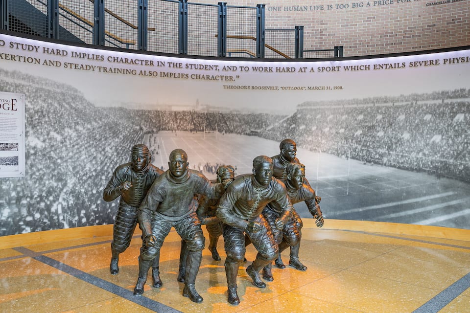 A bronze statue of hockey players on a rink with a banner and a plaque in the background.