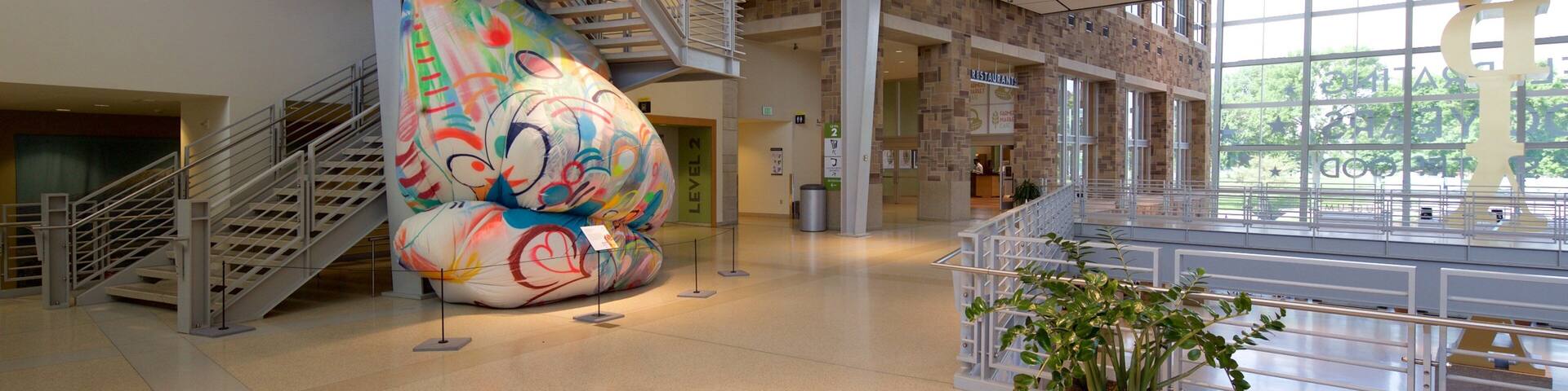 A modern building with a large, colorful sculpture, multiple staircases, and a spacious atrium.