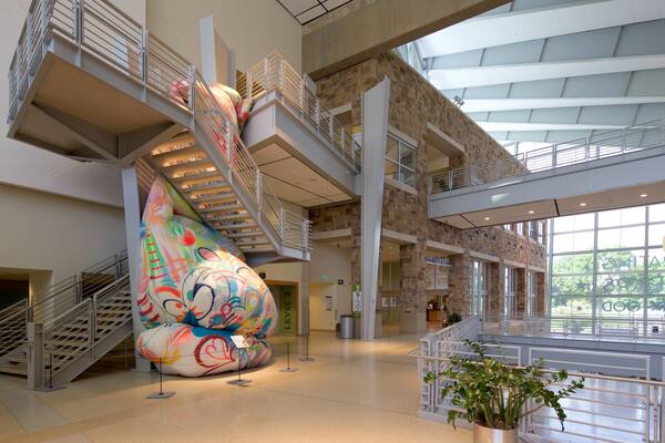 Ein modernes Gebäude mit einer großen, farbenfrohen Skulptur, mehreren Treppenhäusern und einem geräumigen Atrium.