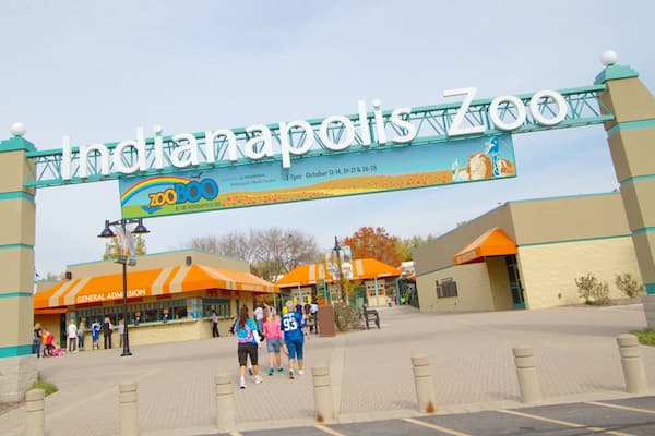 A entrada do Zoológico de Indianápolis, com uma placa grande e um estacionamento.