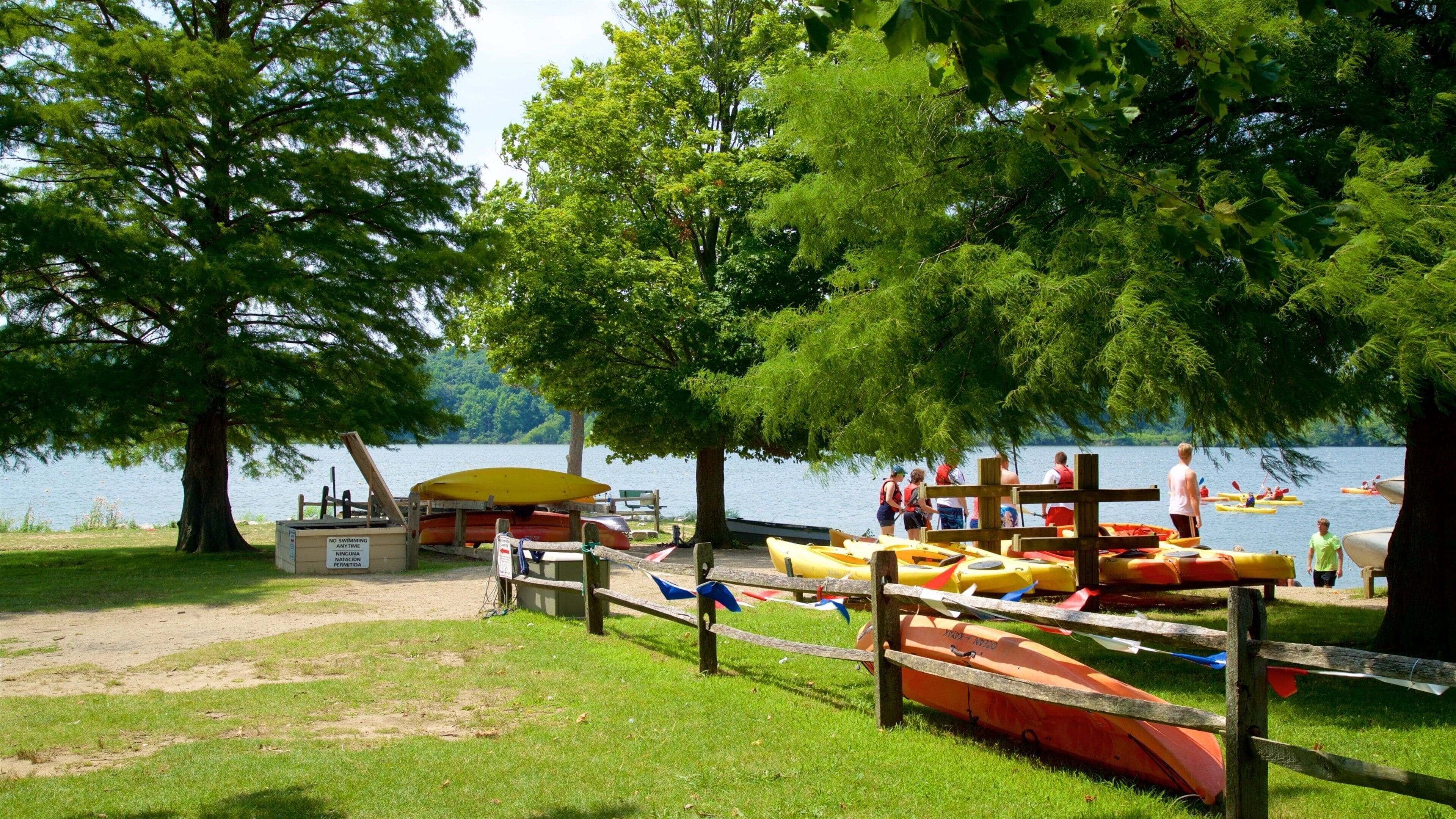 Caserío junto al lago con canoas y kayaks, una valla de madera y un cartel que prohíbe bañarse.