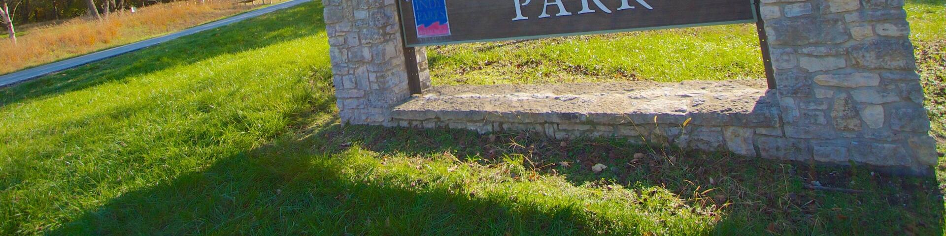 A stone sign with 'Eagle Creek Park' written on it, surrounded by grass and trees with autumn leaves.